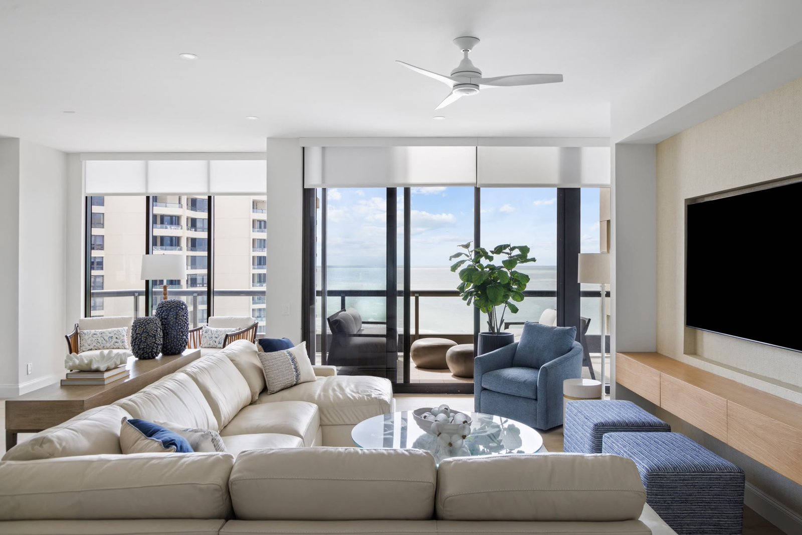 Water Club living room with cream seating, gulf-facing glass, recessed lights, and a ceiling fan hung from the slab, Longboat Key